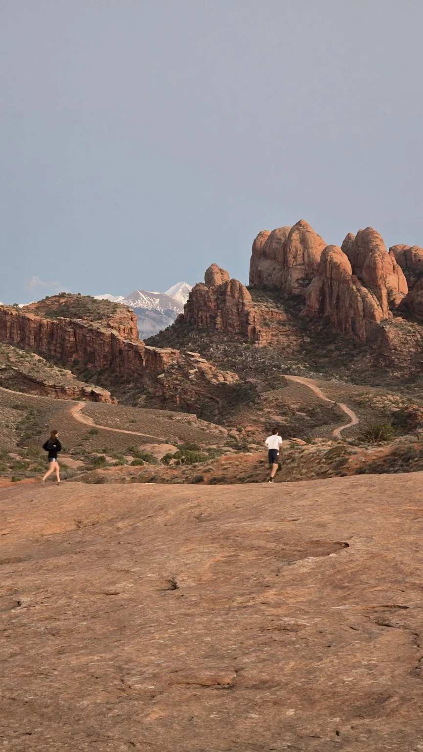 Runners crossing open slickrock below sandstone towers