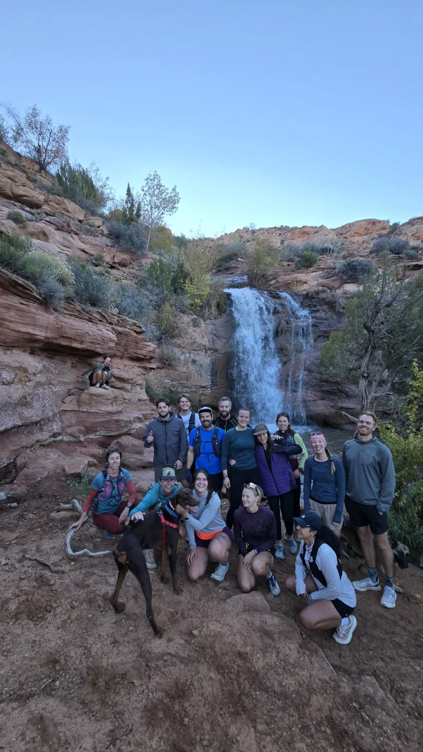 Runners gathered beside a waterfall in a sandstone canyon